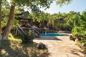 A pool area with stone flooring, a wooden deck, and a building with a covered patio. - Elewana Serengeti Migration Camp (Serengeti)