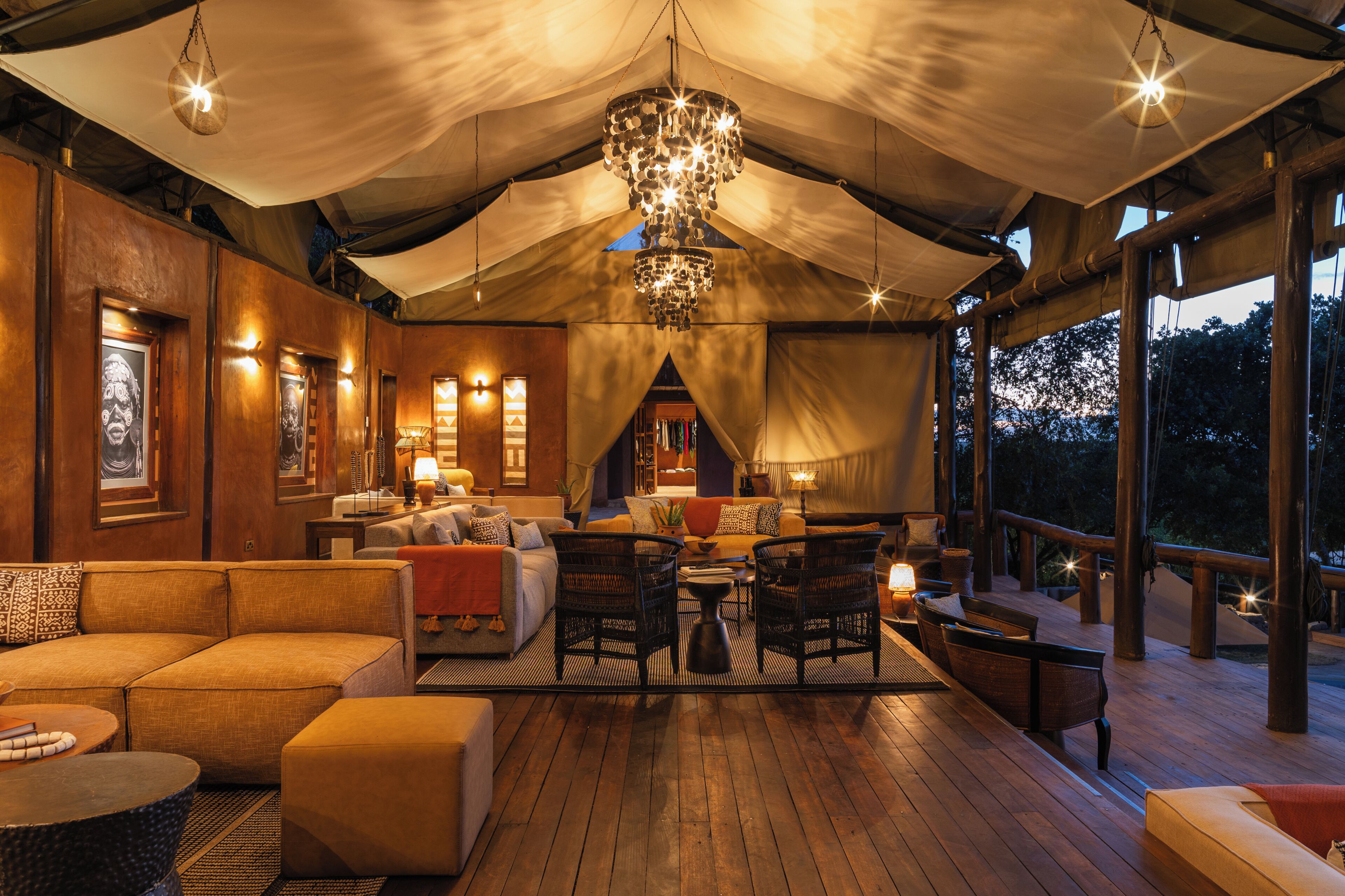 A tented outdoor lounge area with seating, a chandelier, and a view of the outdoors.