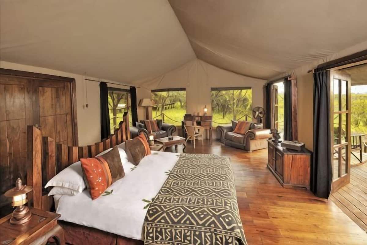 A tented room with a bed, wooden furniture, and large windows.