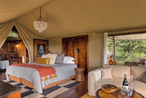 A tented accommodation with a bed, a sofa, a dining area, and a view of the outdoors.