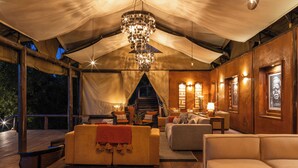 A tented room with a chandelier, sofas, a fireplace, and a staircase. - Elewana Serengeti Migration Camp (Serengeti)