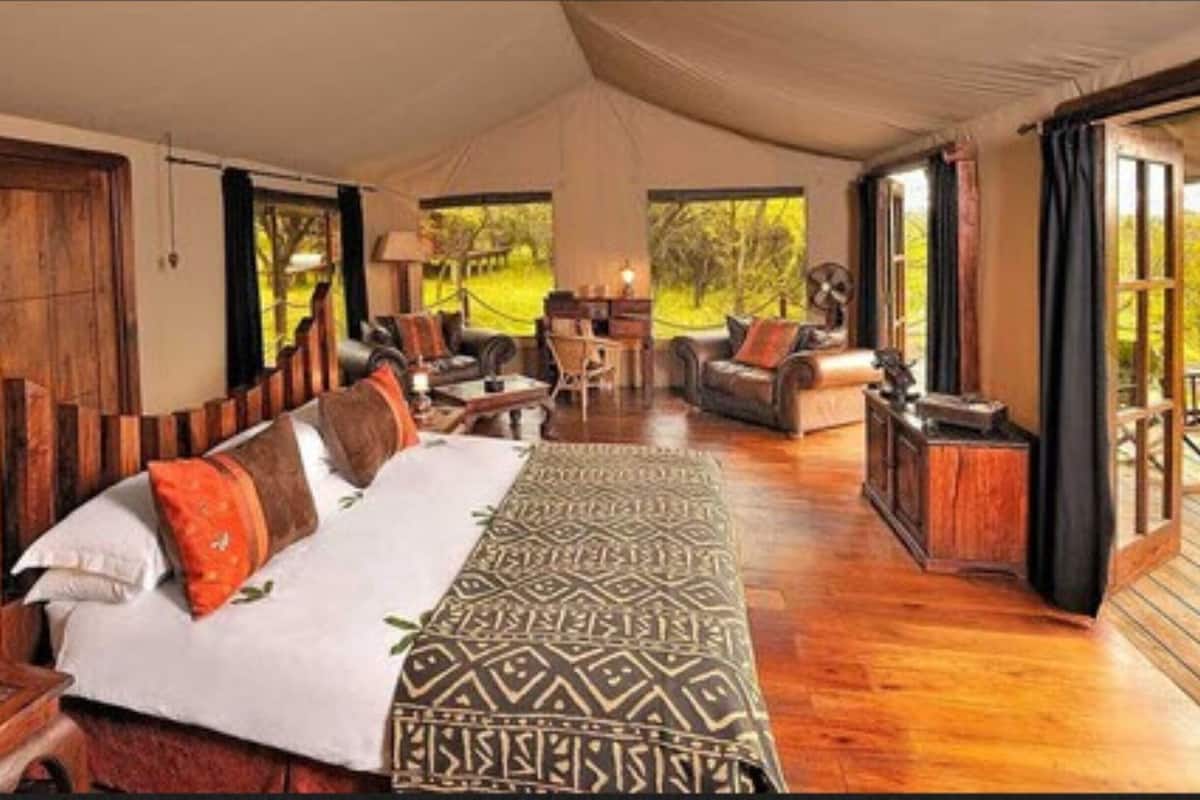 A tented room with a bed, seating area, and large windows.