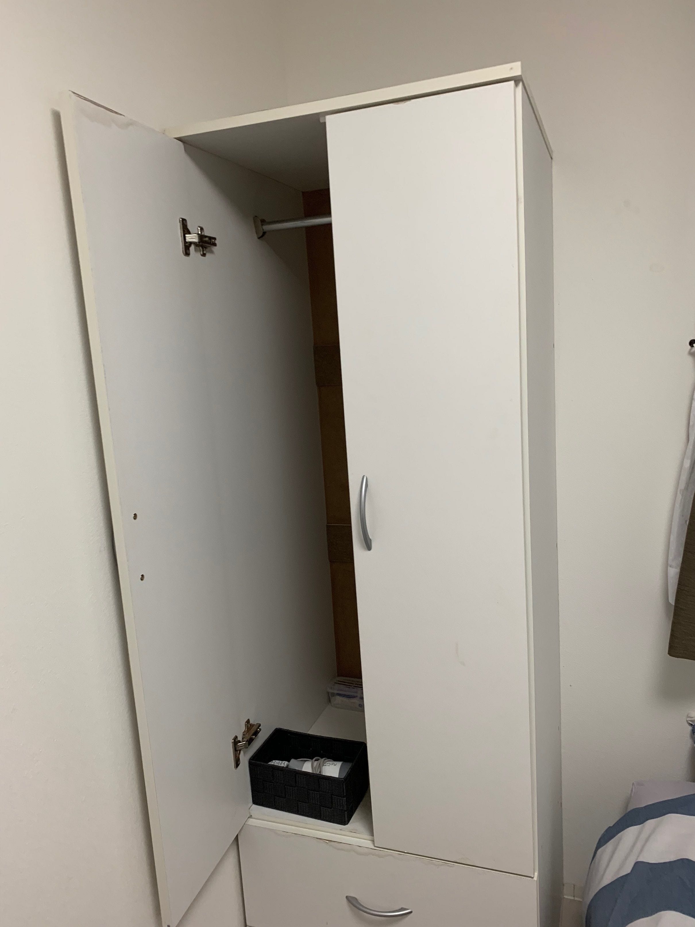 A white wardrobe with a handle, a black storage box, and a small drawer.
