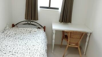 A bedroom with a bed, a white desk, and a window with curtains.