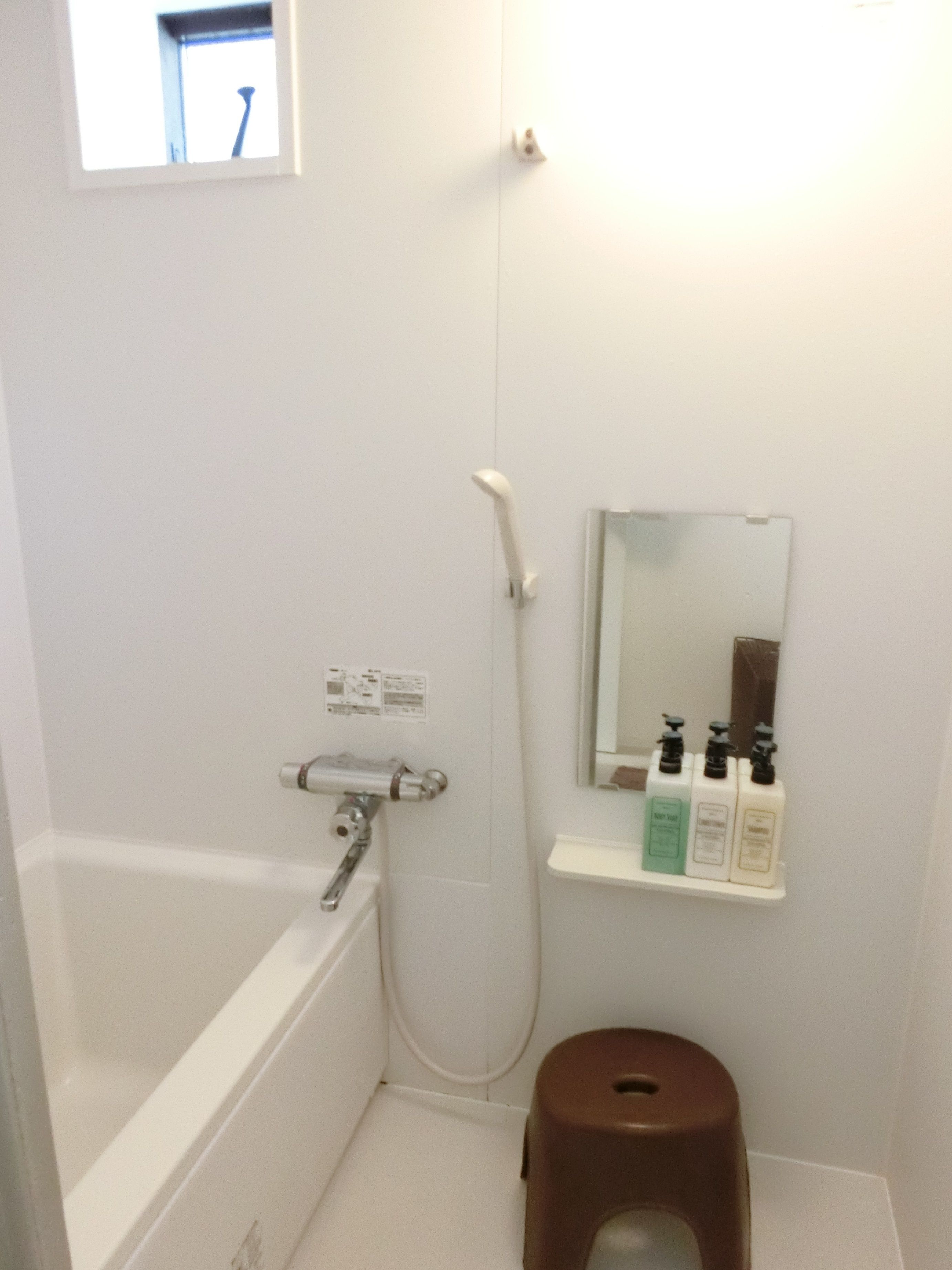 A small bathroom with a white bathtub, a shower, a toilet, and a shelf with toiletries.