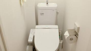 Ein kleines, weißes Badezimmer mit Toilette, Papierhalter und Mülleimer.