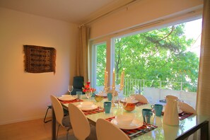A dining area with a table set for four, a window with a view of trees, and a wall hanging. - Wonderful Helsinki Apartment (Helsinki)