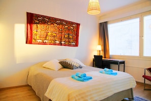 A neatly made bed with blue towels, a tapestry on the wall, and a window with curtains. - Wonderful Helsinki Apartment (Helsinki)