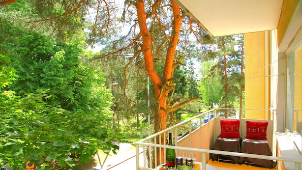 A balcony with a view of a tree-lined street, a car parked outside, and a table with bottles and glasses. - Wonderful Helsinki Apartment (Helsinki)