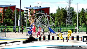 A playground with a large Ferris wheel, a fenced area, and buildings in the background. - Wonderful Helsinki Apartment (Helsinki)