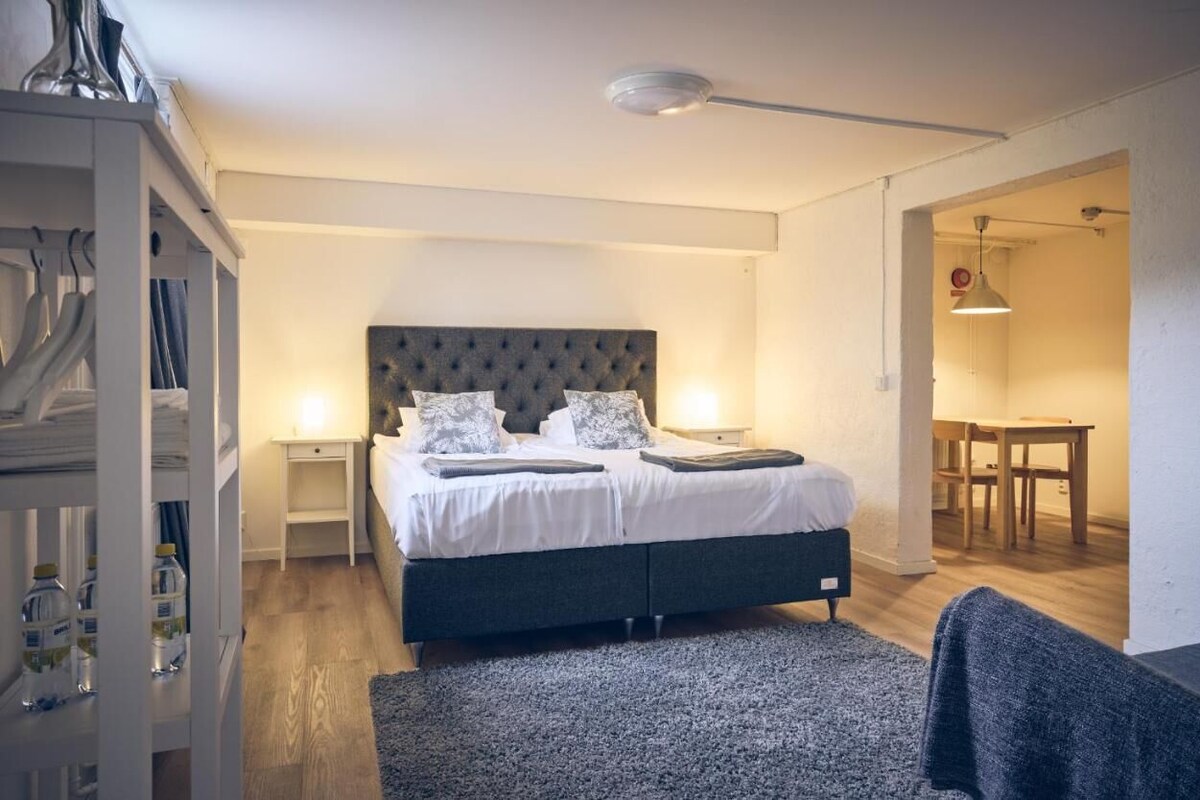 A bedroom with a large bed, bedside tables, a wardrobe, and a dining area with a table and chairs.