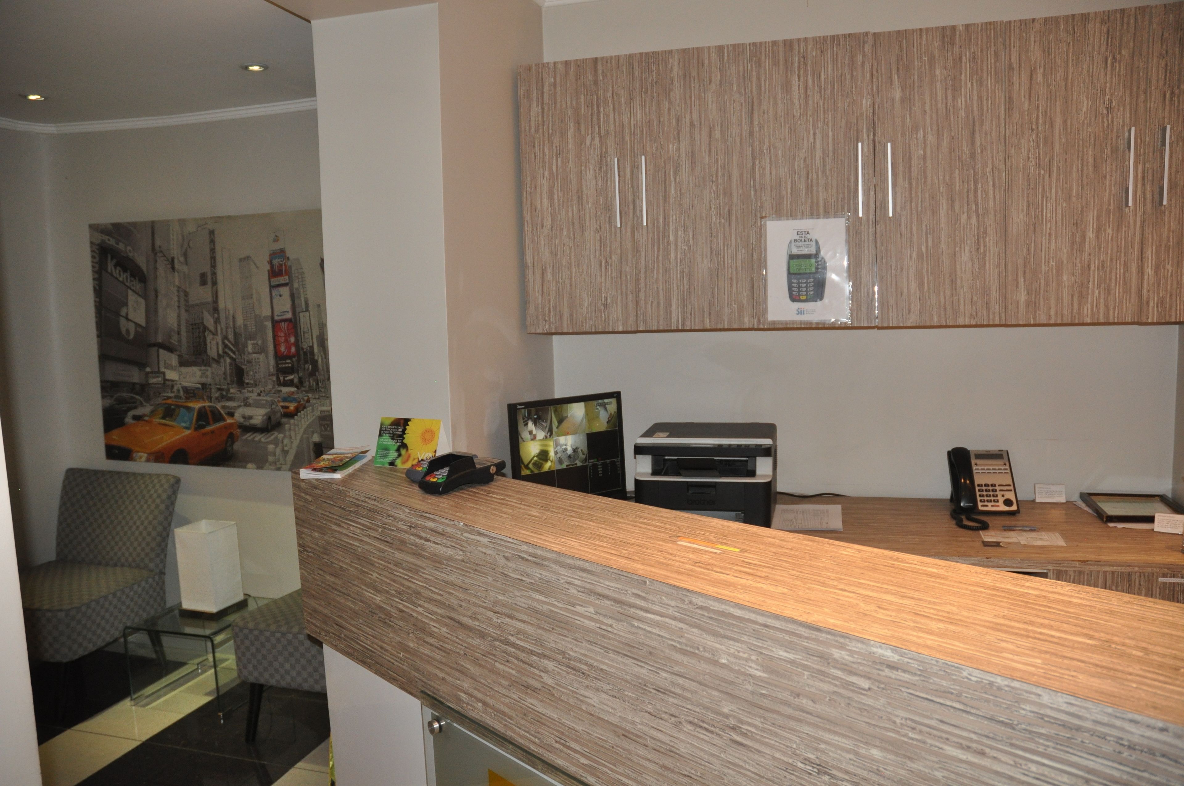 A reception desk with a wooden finish, a telephone, a printer, and a framed picture of a cityscape.