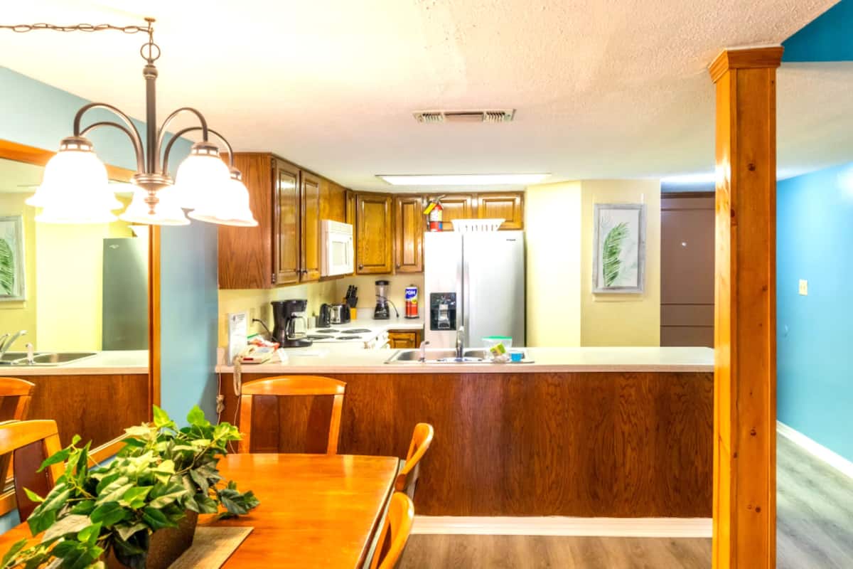 A kitchen with wooden cabinets, a central island, and a dining area with chairs.
