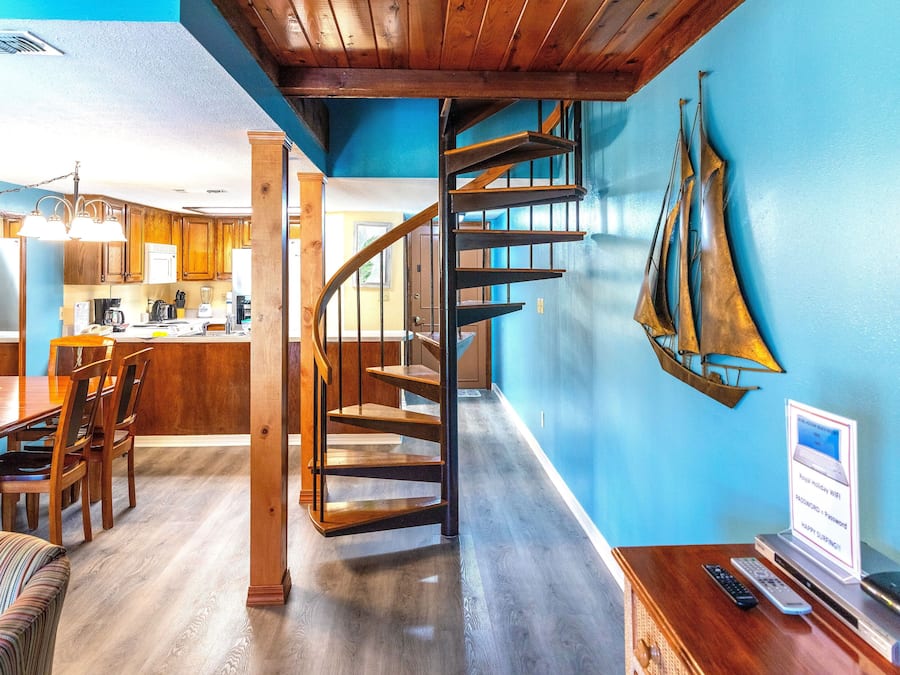 Une cuisine moderne avec des meubles en bois, un coin repas doté d’un canapé à rayures et un escalier en colimaçon menant à un autre niveau.