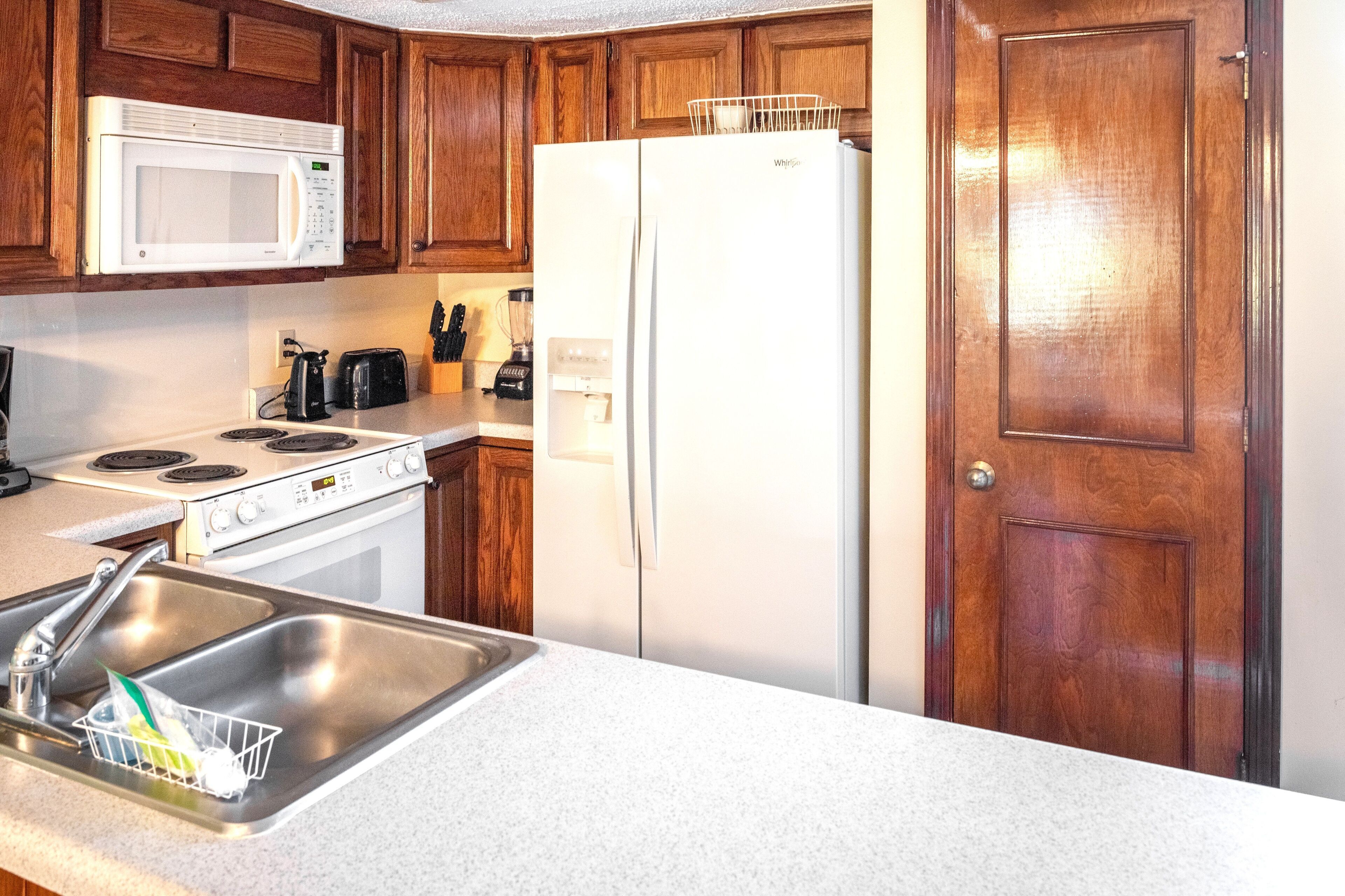 Una cucina con mobili in legno, un forno a microonde bianco, un frigorifero bianco, un fornello e un lavello con scolapiatti.