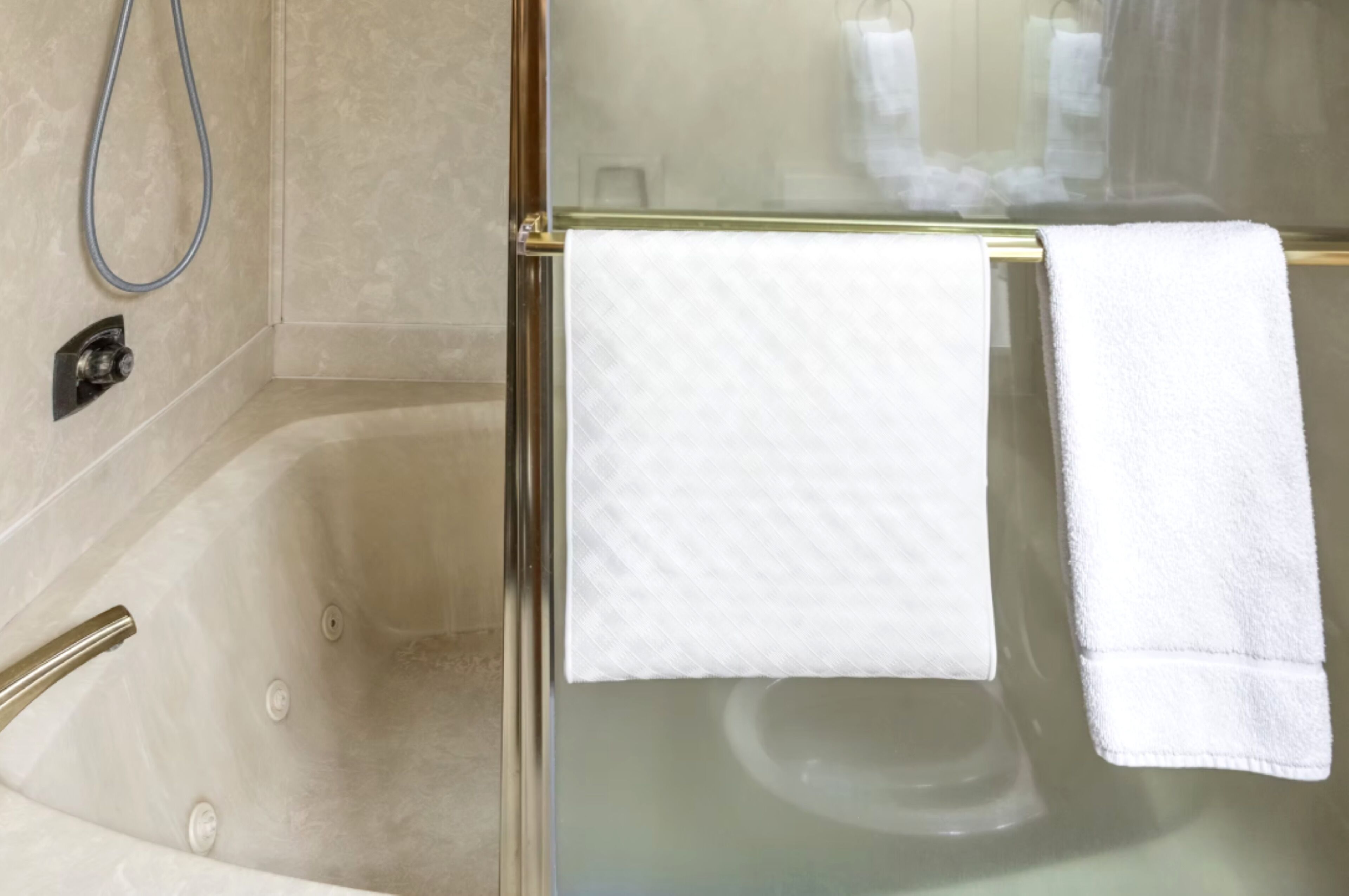 Un espace douche entièrement vitré, avec une serviette blanche suspendue à une barre à serviettes dorée.