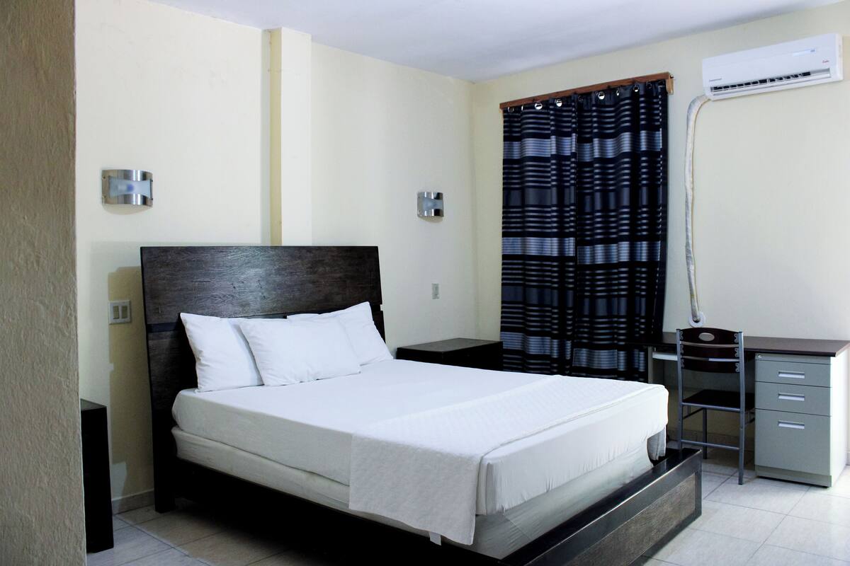 A bedroom with a bed, a desk, and an air conditioning unit.