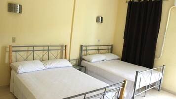 Una habitación con dos camas individuales, una ventana con cortinas negras y una lámpara fijada a la pared.
