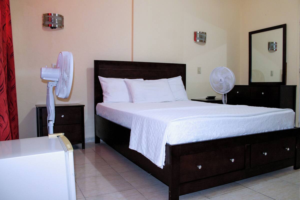 A neatly made bed with white linens, a wooden headboard, and two bedside tables with fans.