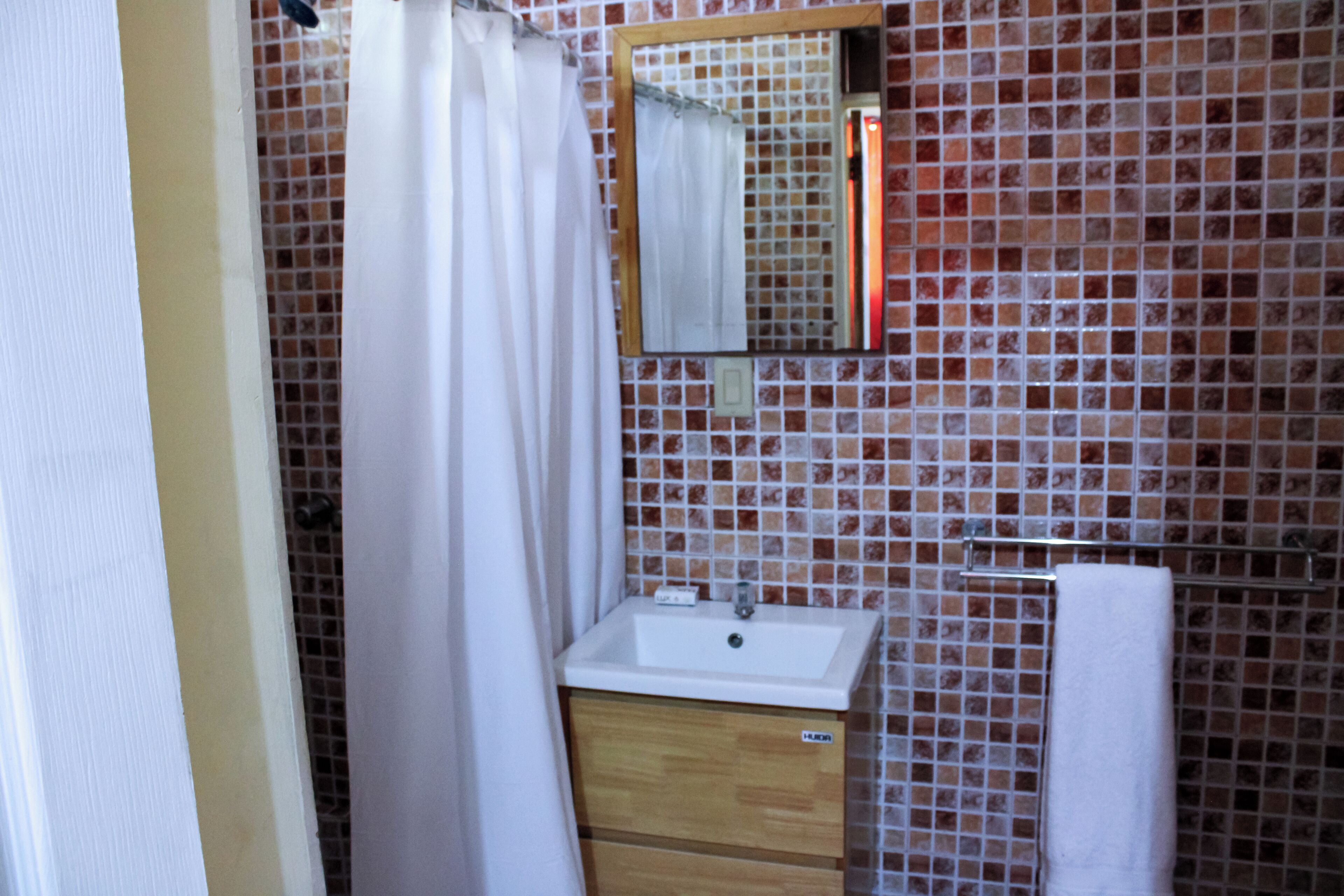 A bathroom with a white sink, wooden cabinet, and a tiled wall.
