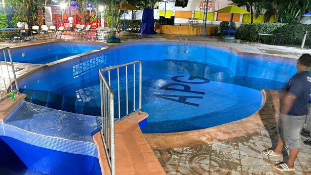 Piscina con interior azul y bordeado de azulejos, rodeada de mobiliario exterior y una zona cubierta.