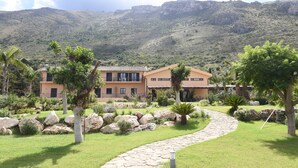 A modern house with a stone pathway, surrounded by lush greenery and large rocks. - Ulivo Blu Casa Vacanze (Castellammare del Golfo)