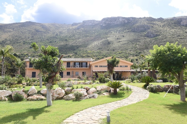 A modern house with a stone pathway, surrounded by lush greenery and large rocks.
