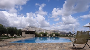 A pool area with lounge chairs, a stone building, and mountains in the background. - Ulivo Blu Casa Vacanze (Castellammare del Golfo)