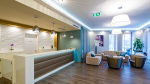 Un área de recepción moderna con un mostrador blanco, varias lámparas colgantes y una zona de estar con sofás y sillones.