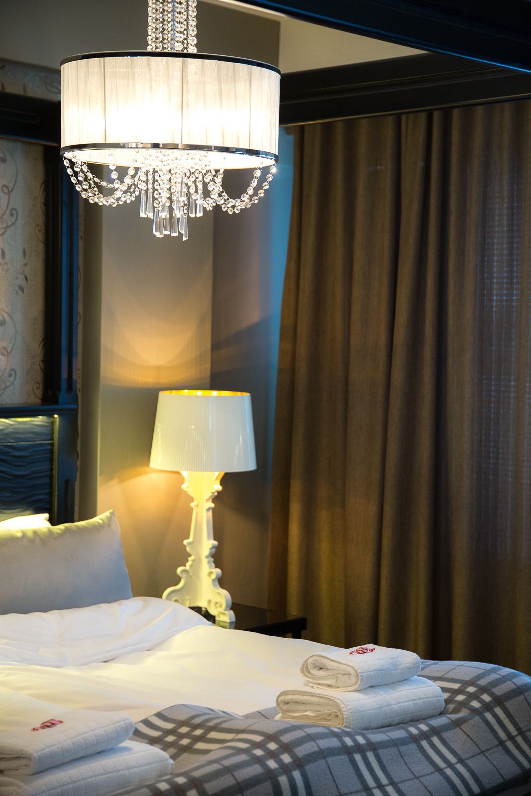 A hotel room with a bed, a chandelier, a lamp, and curtains.