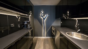 A modern kitchen with dark cabinetry, a central light fixture, and a stainless steel sink. - Hotel Olof (Tornio)