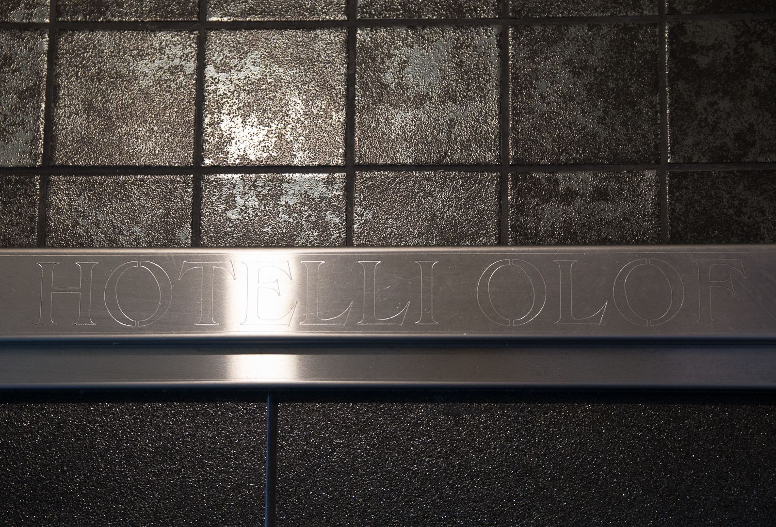 A metallic sign with the inscription "HOTELIOLOF" on a tiled wall.