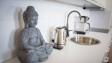 A kitchen with a Buddha statue, a kettle, and a sink.