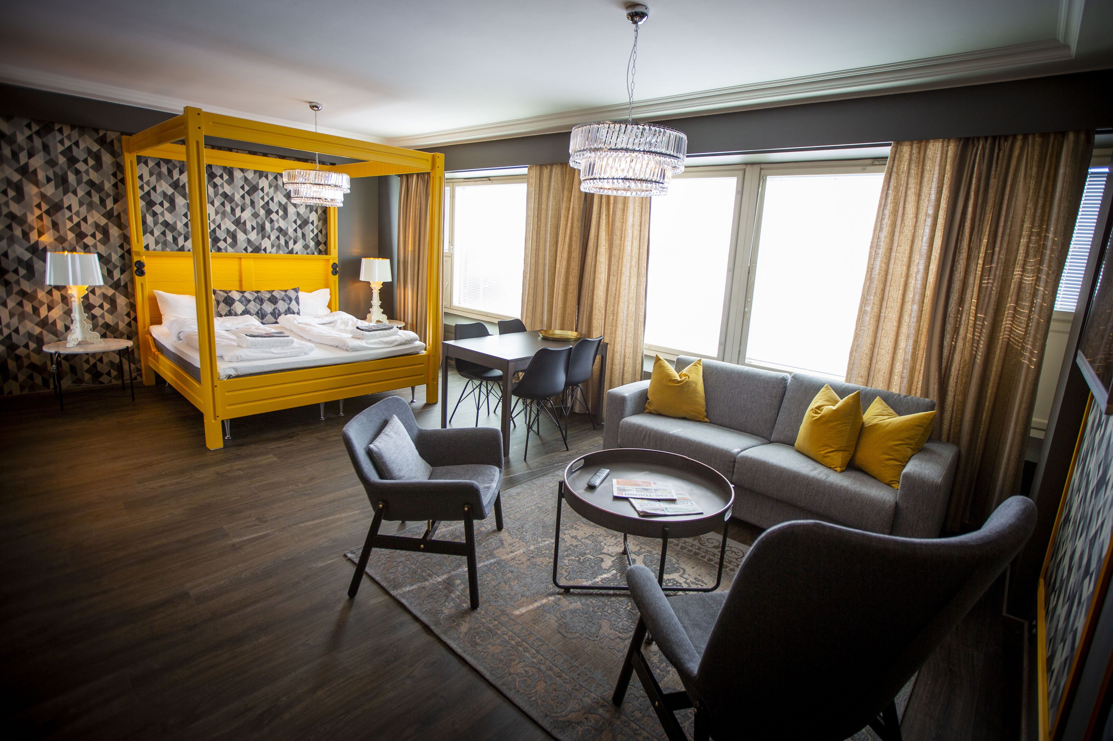 A hotel room with a four-poster bed, a sofa, a coffee table, and a dining area.