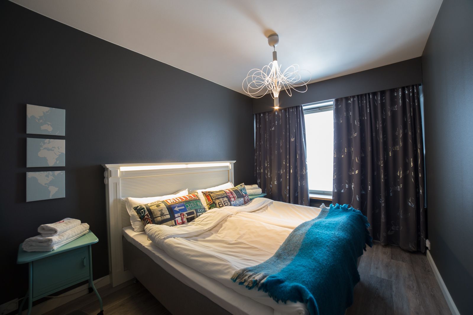 Un dormitorio moderno con una cama, una mesita de noche con lámpara, una ventana con cortinas y decoración en la pared.