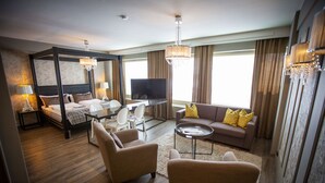 A four-poster bed with a television, a sofa with yellow pillows, and a coffee table in a well-lit room with a chandelier. - Hotel Olof (Tornio)