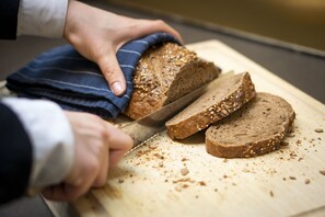 Uma pessoa cortando uma fatia de pão com sementes em uma tábua de madeira.