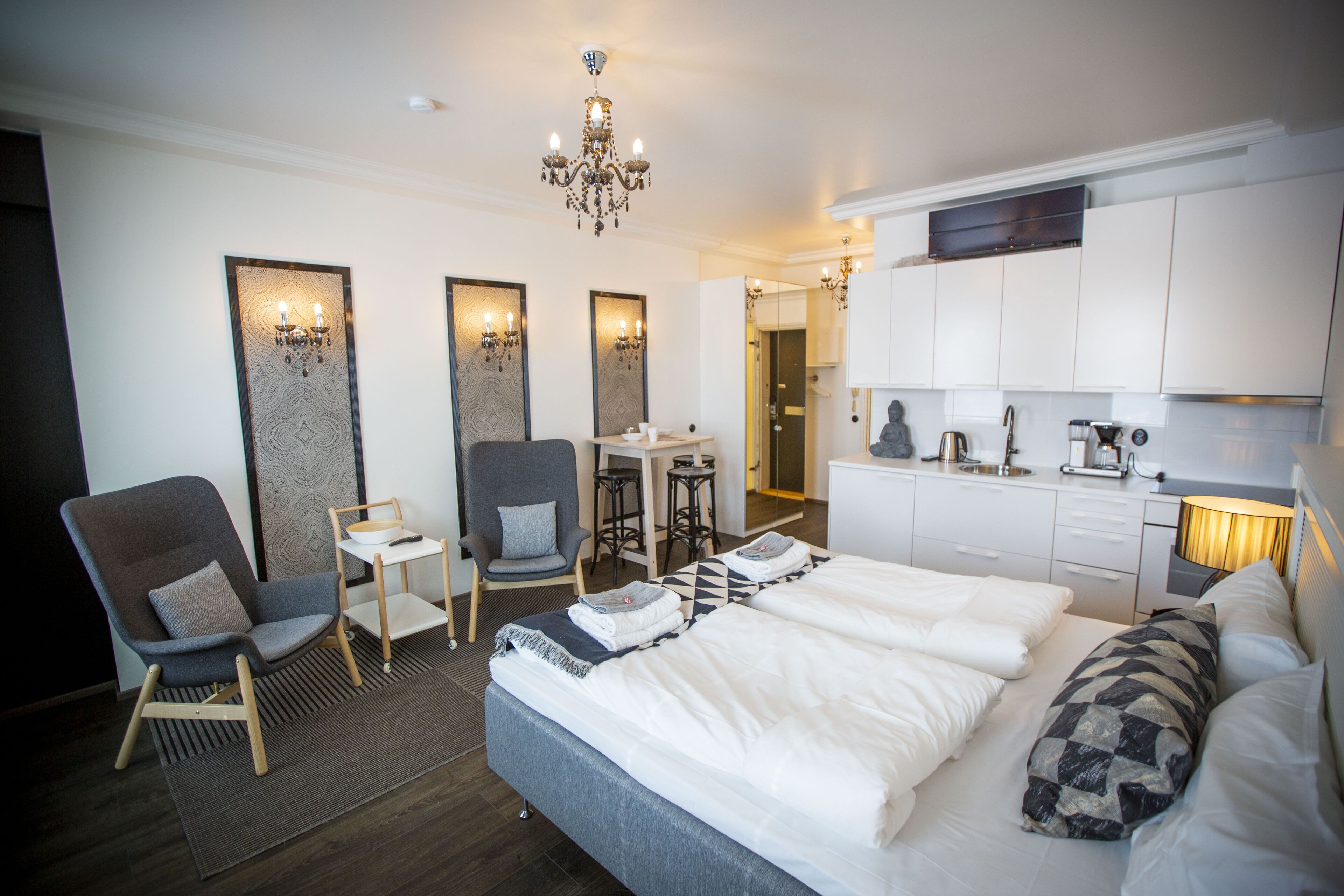 Una habitación de hotel moderna con una cama grande, dos sillones, un escritorio pequeño y una kitchenette.