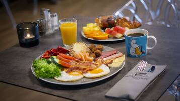 A breakfast table with plates of eggs, bacon, sausages, and toast, a glass of orange juice, and a coffee cup.