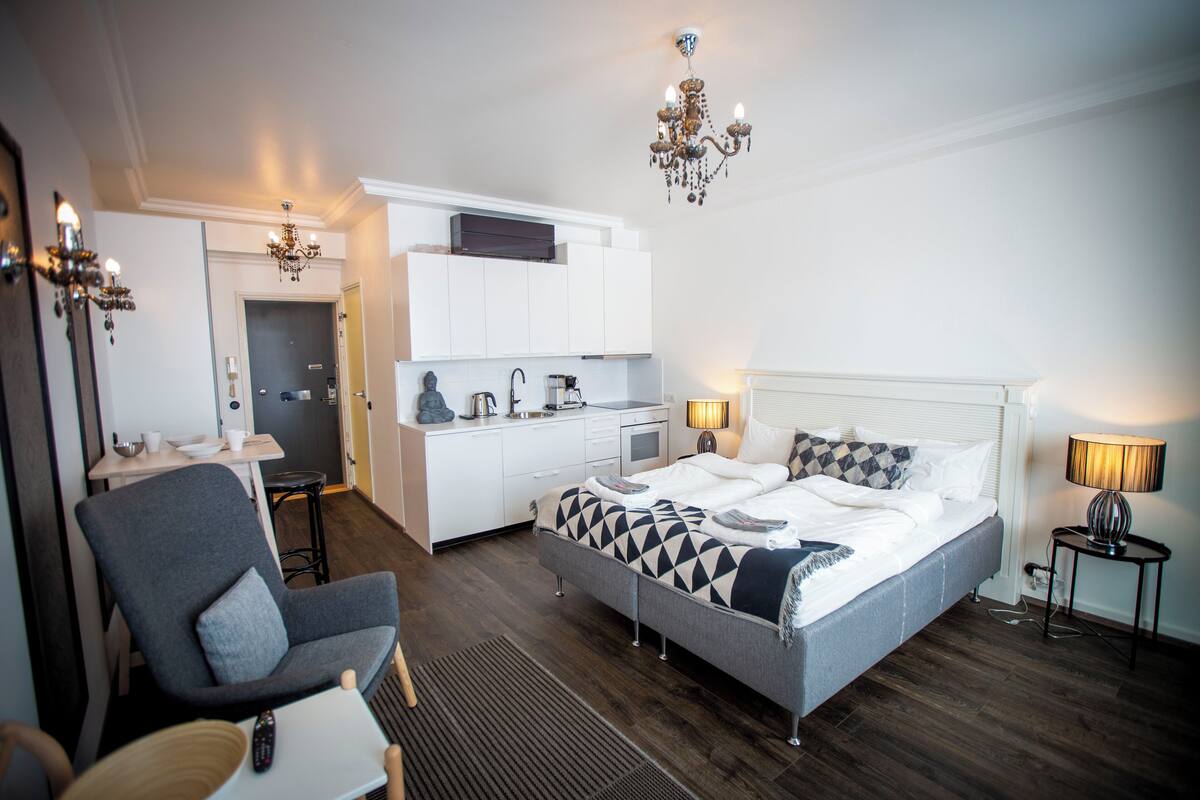 A modern hotel room with a bed, a small kitchenette, a dining area, and a separate seating area.