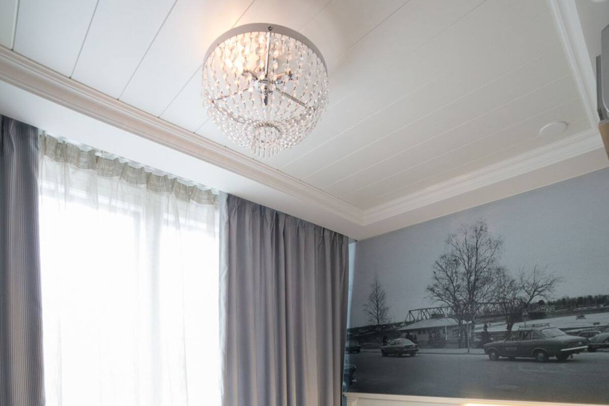A hotel room with a large bed, a chandelier, a painting of a landscape, and a view of a parking lot.