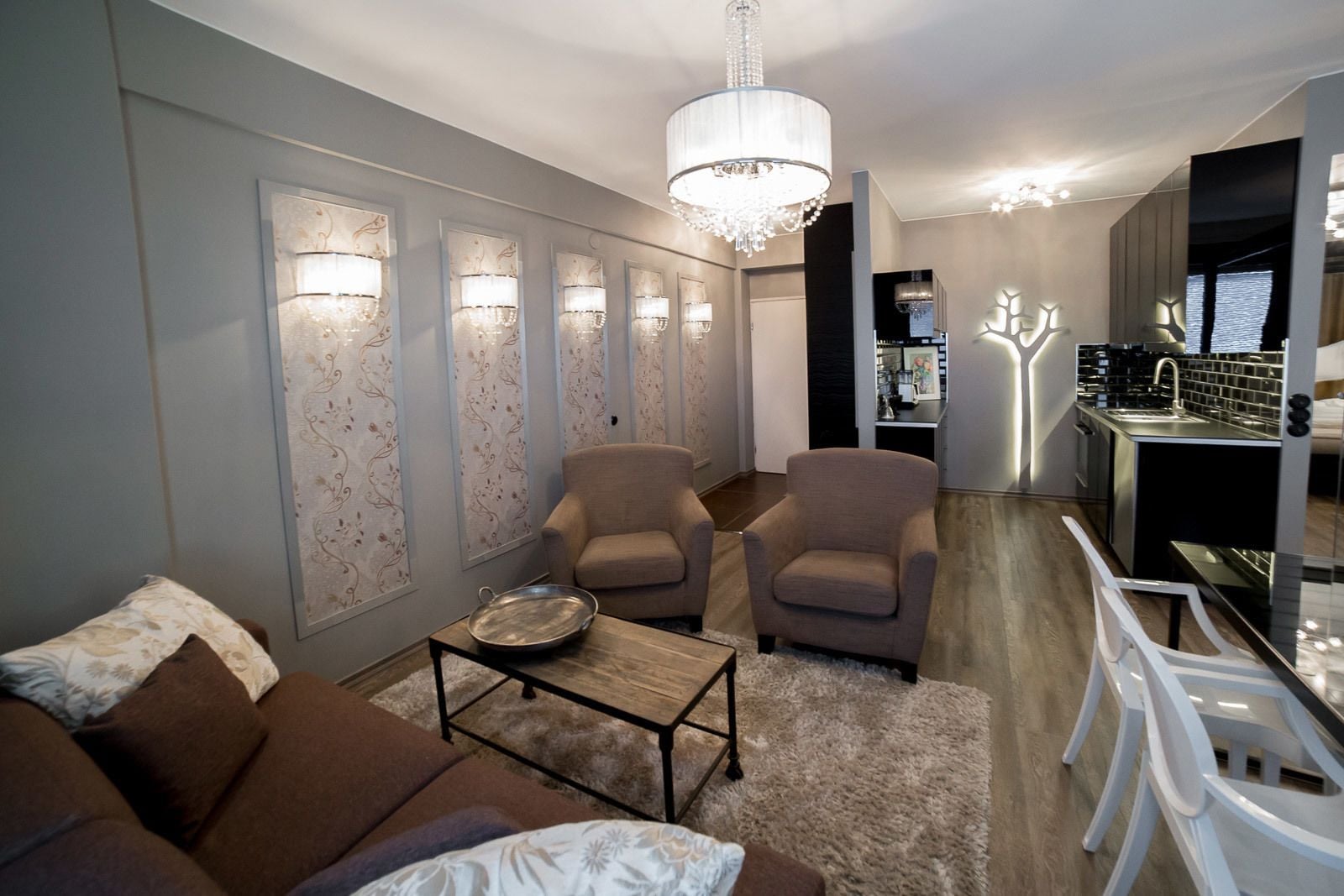 A modern living room with a sofa, two armchairs, a coffee table, and a chandelier.