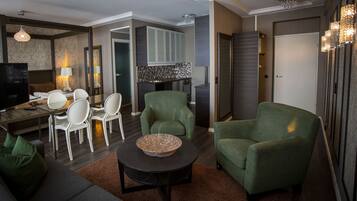 Una sala moderna con un sofá, dos sillones verdes, una mesa de comedor con sillas, un televisor y una cocina con armarios y encimera.