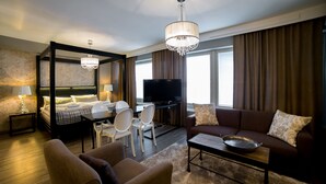 A modern hotel room with a four-poster bed, a television, a sofa, and a dining area with chairs. - Hotel Olof (Tornio)