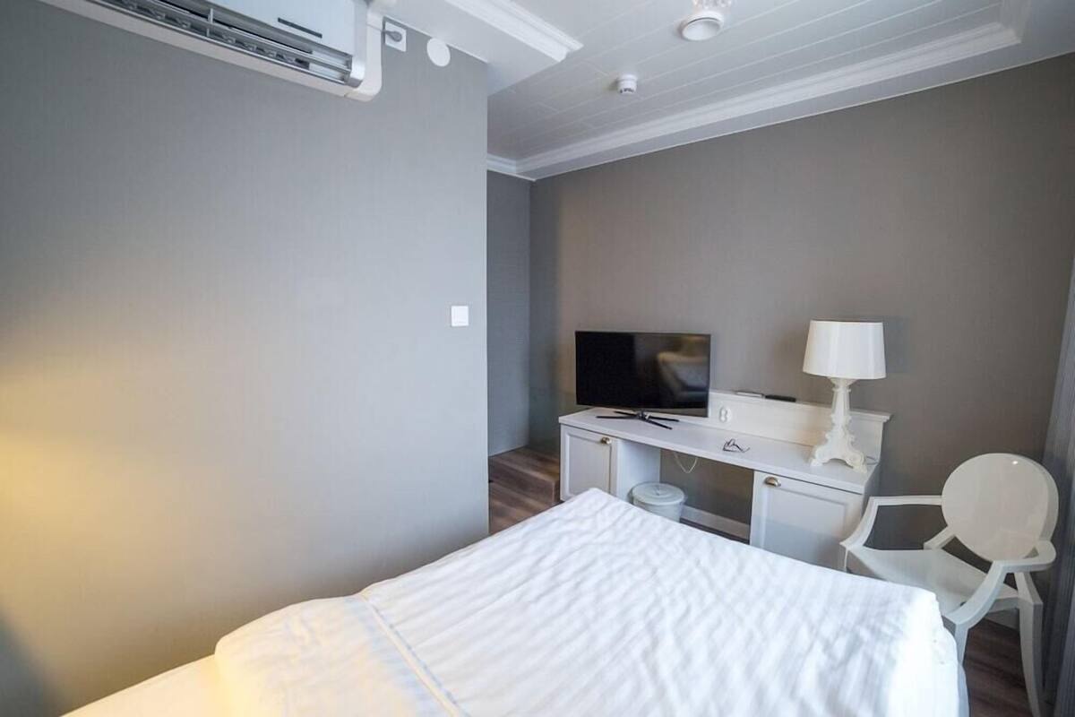 A hotel room with a bed, a desk with a TV, a chair, and a lamp.
