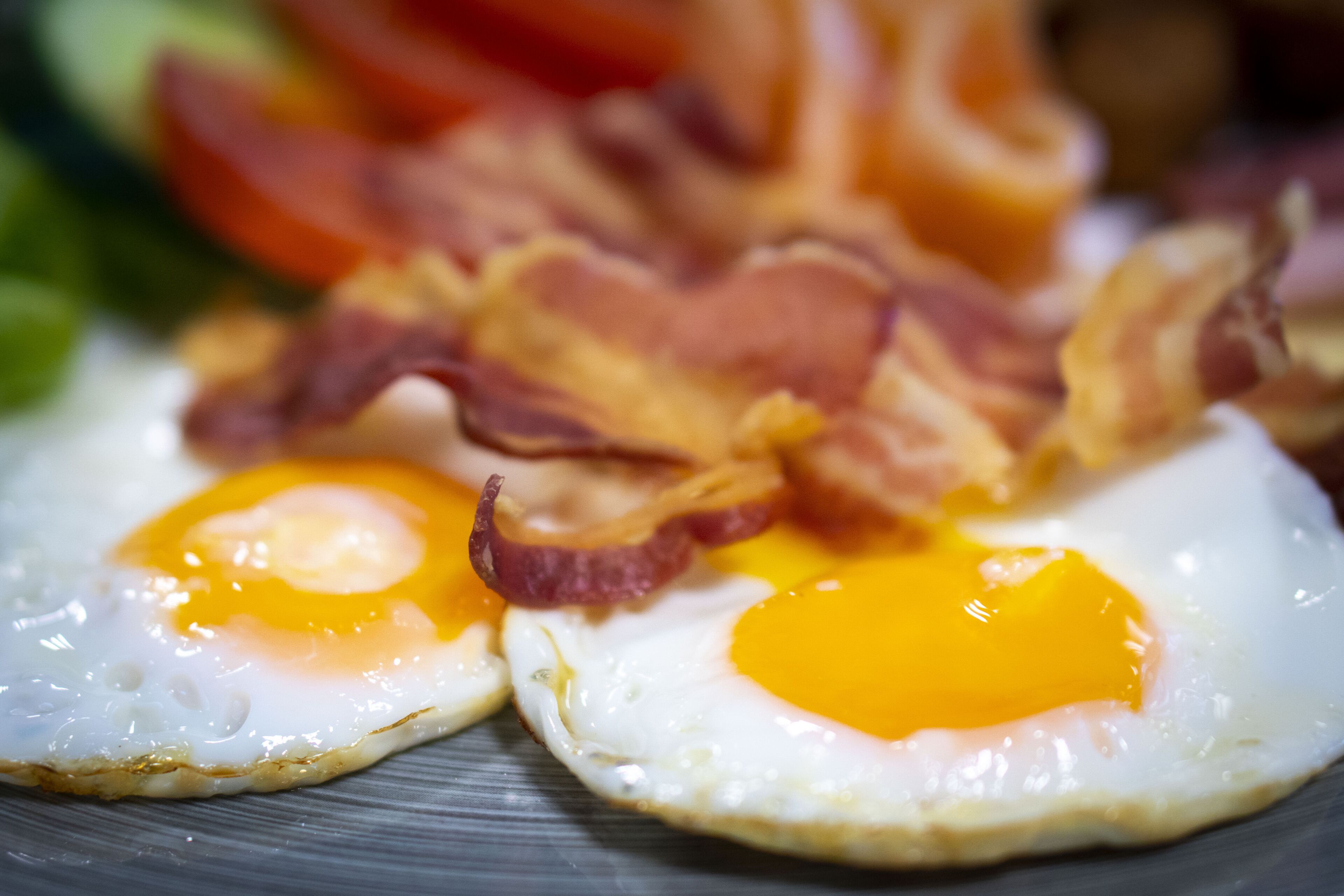 Two sunny-side-up eggs on a plate with bacon strips and a slice of tomato.