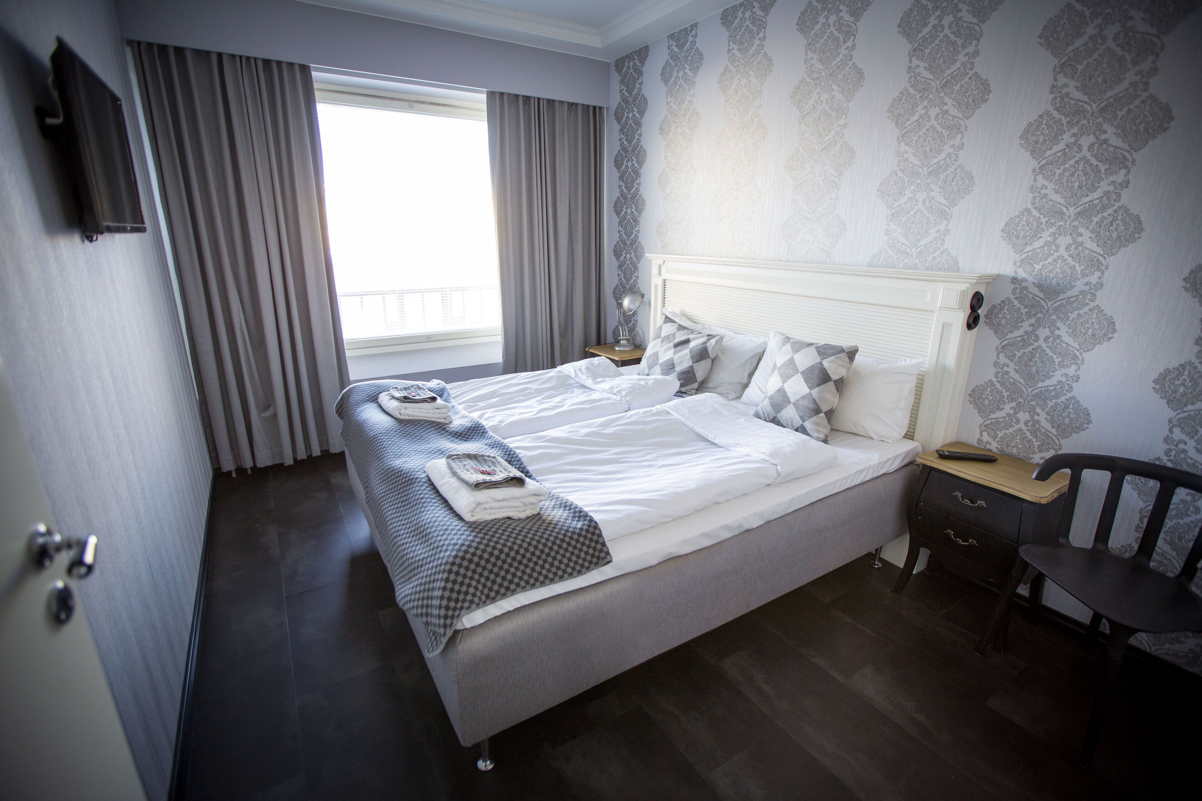A neatly made bed with pillows and a blanket, a bedside table with a lamp, and a chair.
