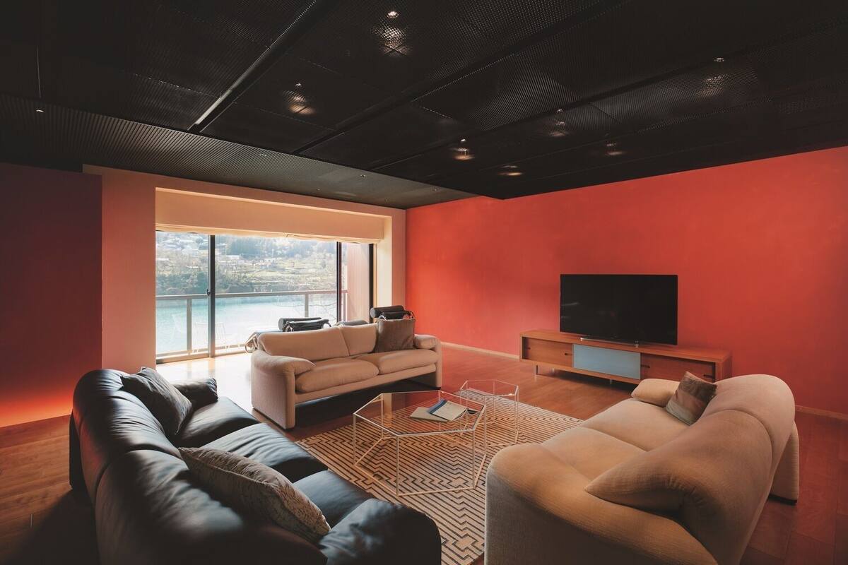 A modern living room with a large window, a flat-screen TV, and leather sofas.