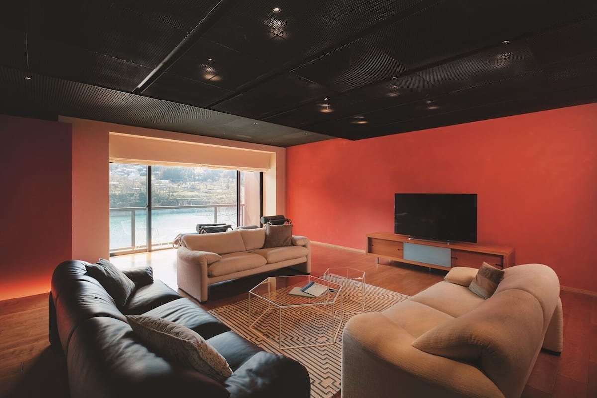 A modern living room with a large window, a flat-screen TV, and leather sofas.