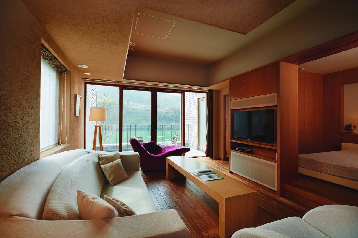 A modern hotel room with a sofa, a small table, a TV, and a balcony with a view.